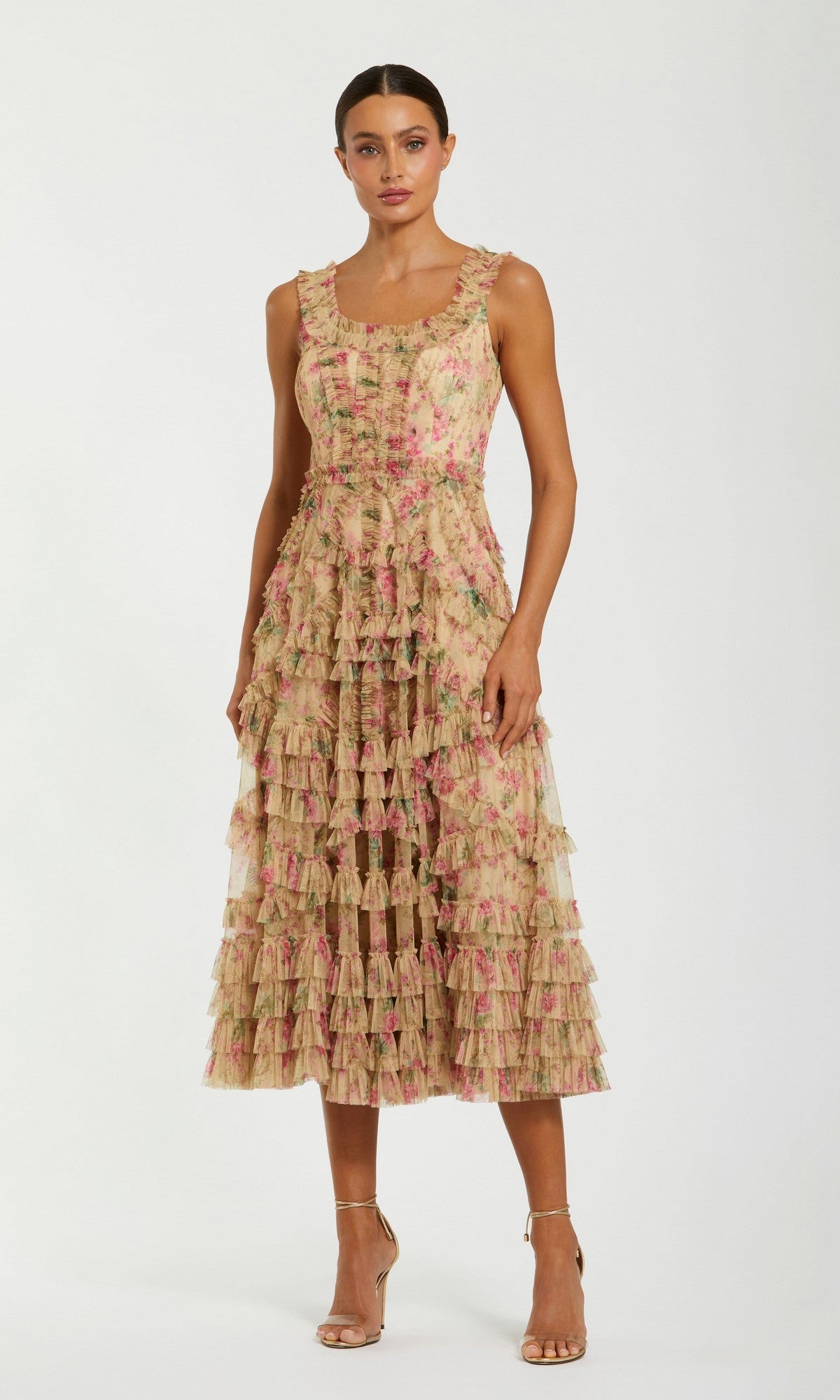 A woman is standing in the Mac Duggal 8293 Midi Party Dress, a sleeveless, beige multi A-line dress with pink floral patterns and layered ruffles, styled with gold high-heeled sandals.